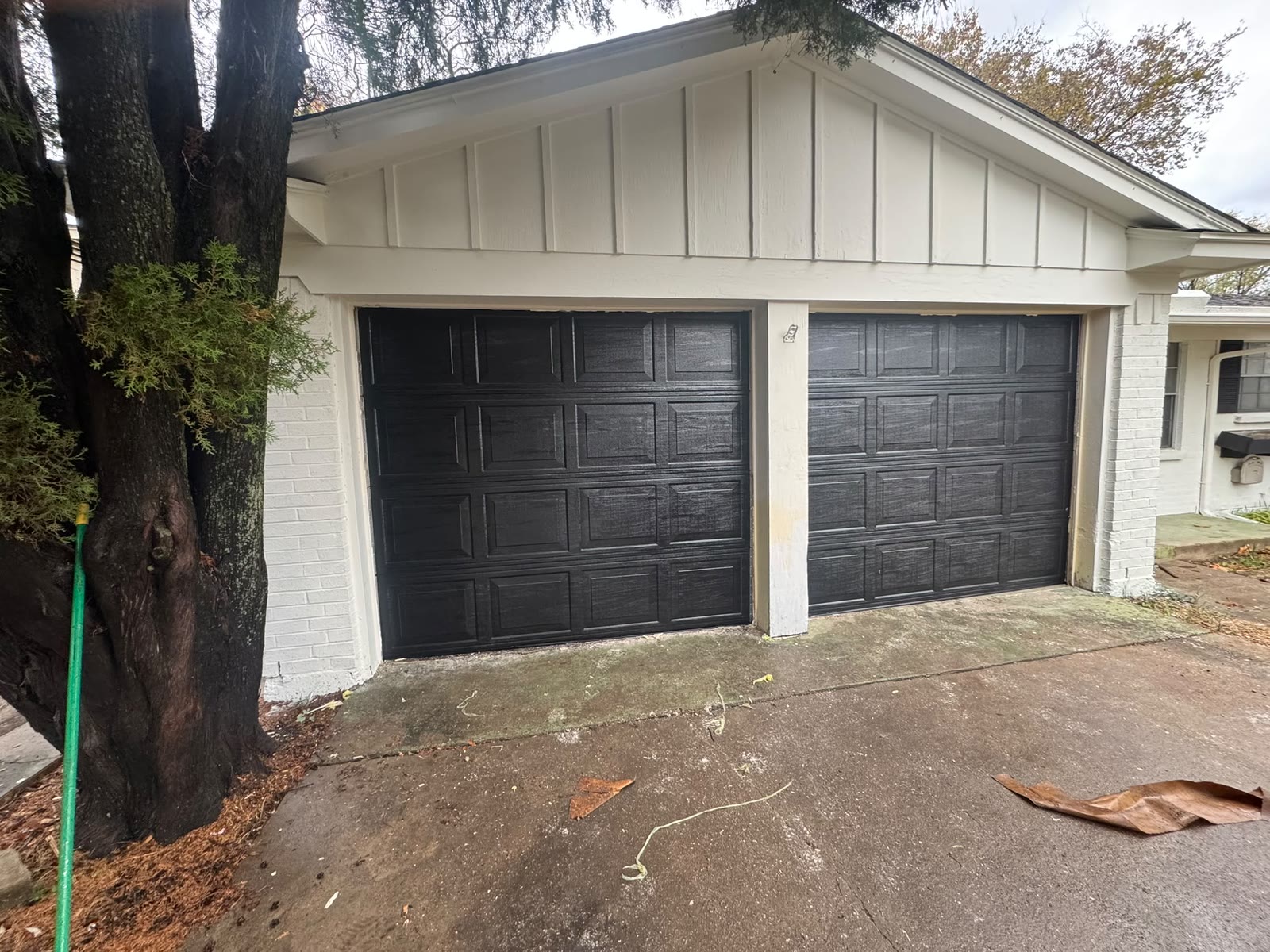 Pair of black short-panel garage doors on a white painted brick home, photographed from the driveway on an overcast day.