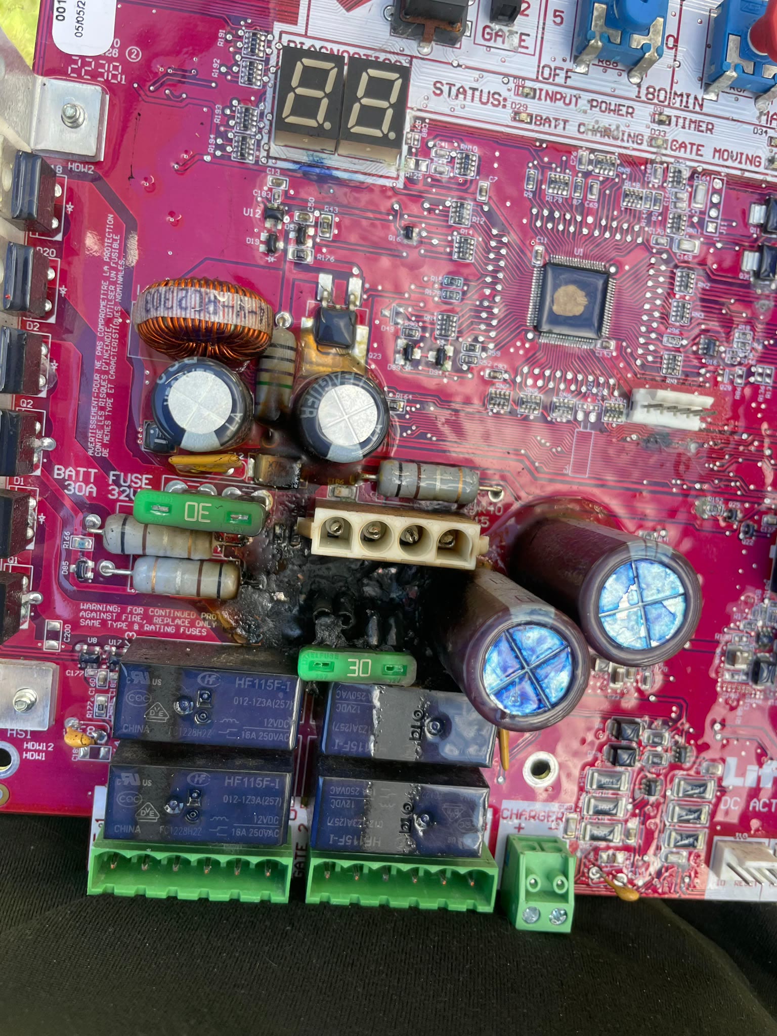 Close-up of a failed operator logic board showing a charred, burnt-through section of the circuit between the relays, with scorched resistors and swollen capacitors alongside.