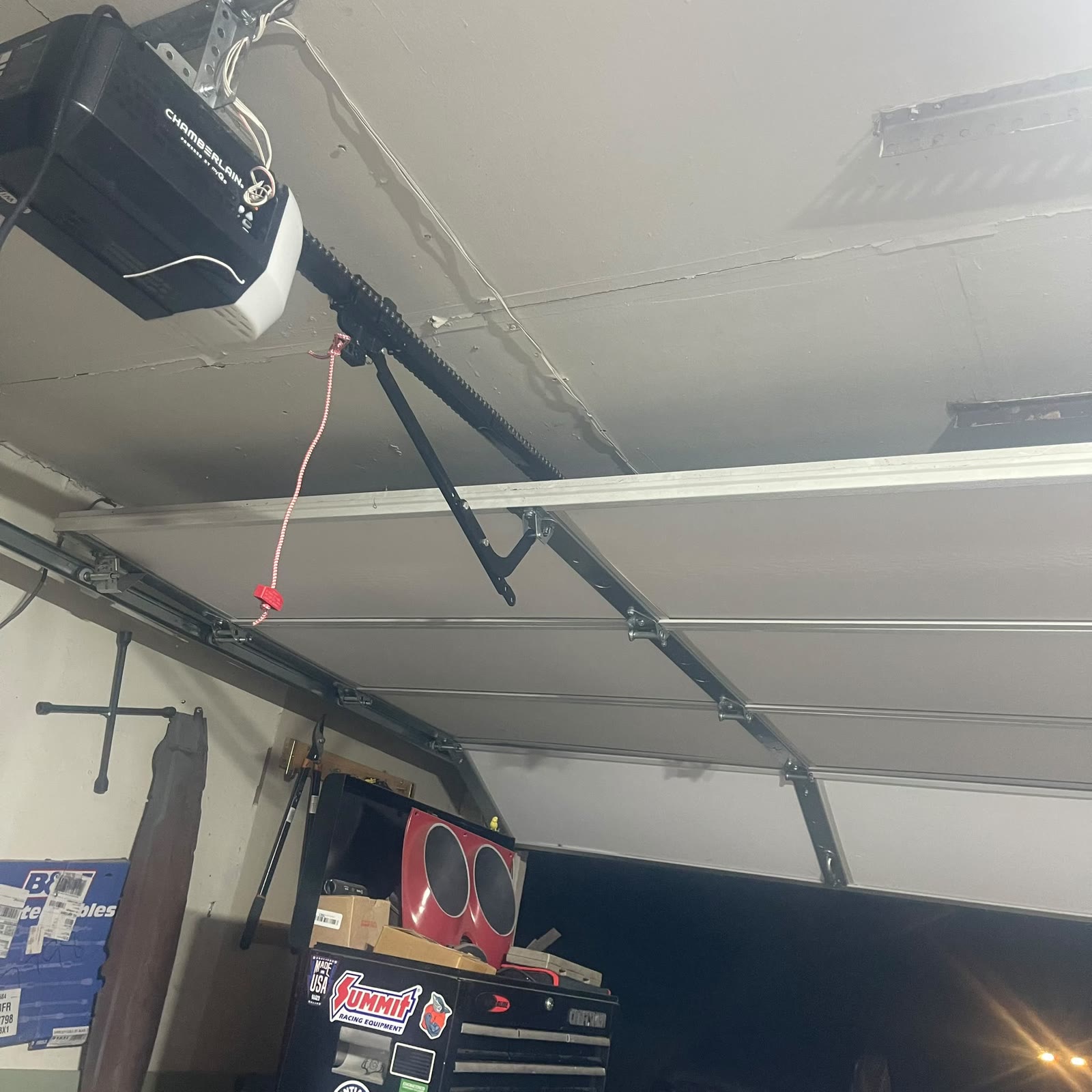 Chamberlain belt-drive opener with its rail, red emergency release cord, curved door arm and horizontal track running the length of a residential garage ceiling.