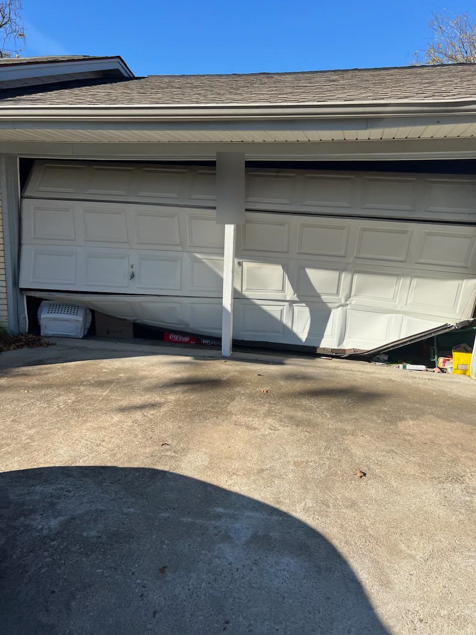 Residential double garage door off its track and buckled into the opening, the right-hand section collapsed down onto stored boxes and the left side still hanging high on its track.