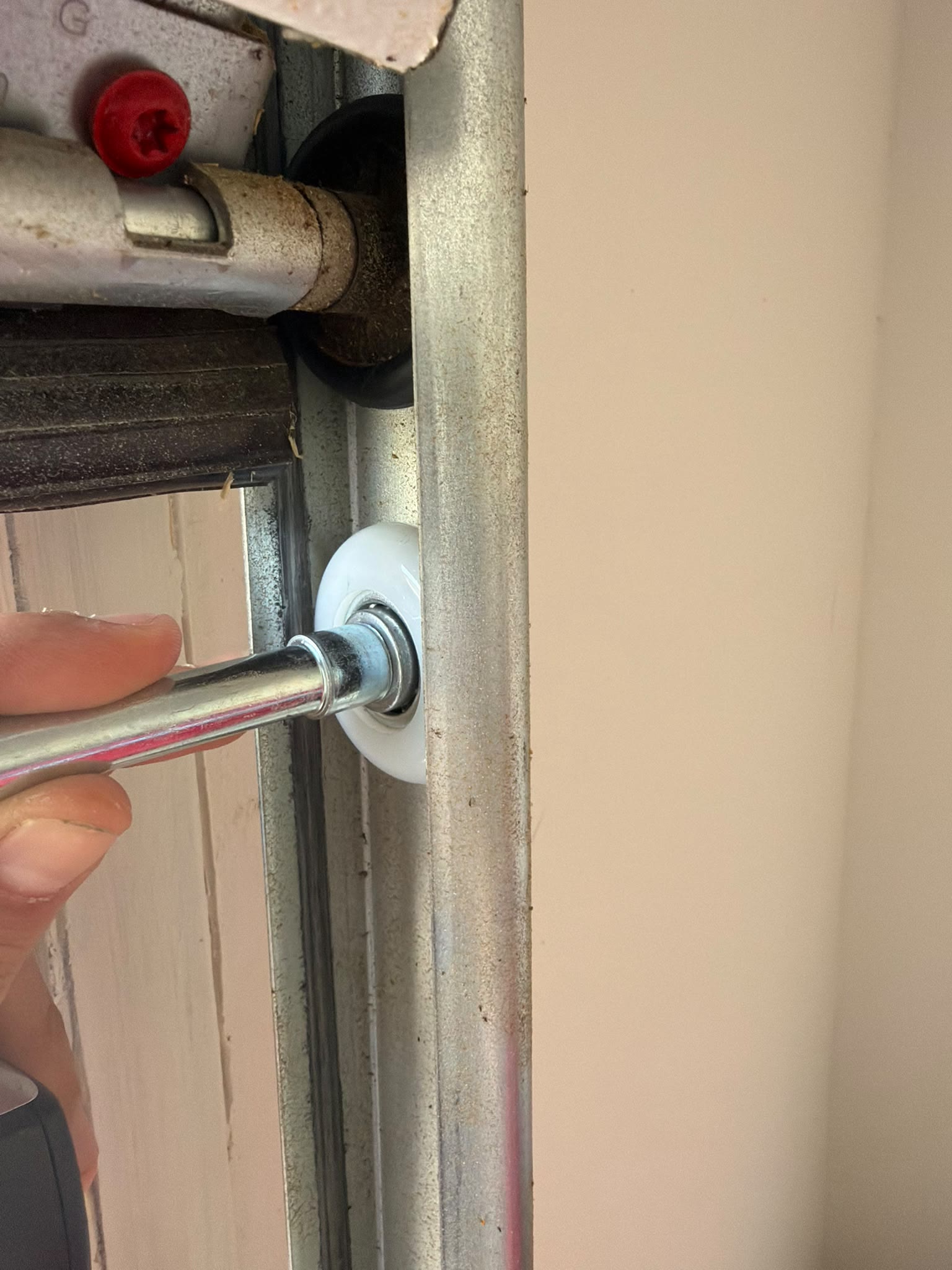 Technician's hand guiding the stem of a new white nylon roller into the vertical track of a garage door, with the old hinge and bracket visible just above.