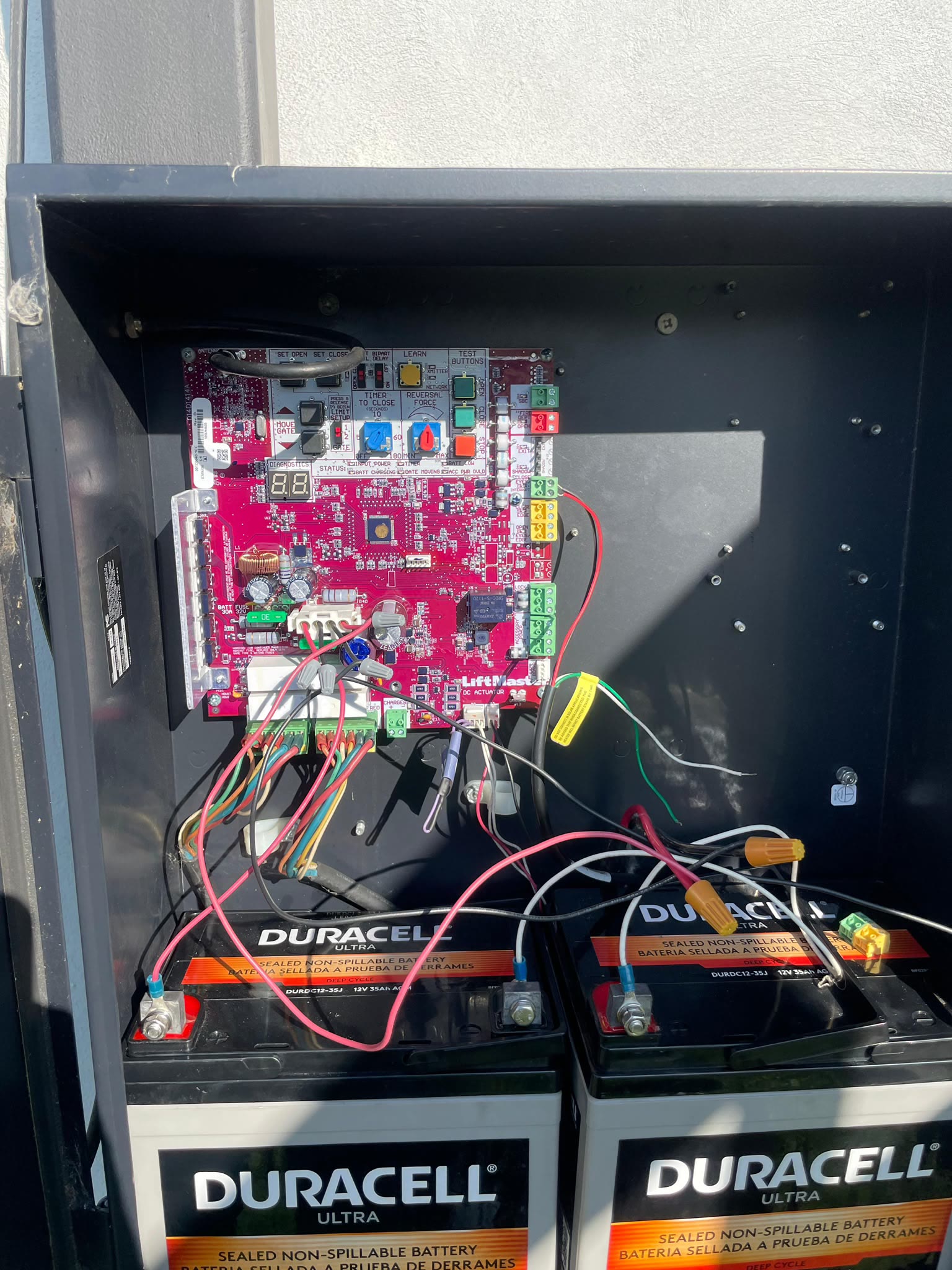 Open control cabinet of a commercial LiftMaster operator, showing the pink logic board with its limit and force dials wired down to two sealed lead-acid backup batteries.